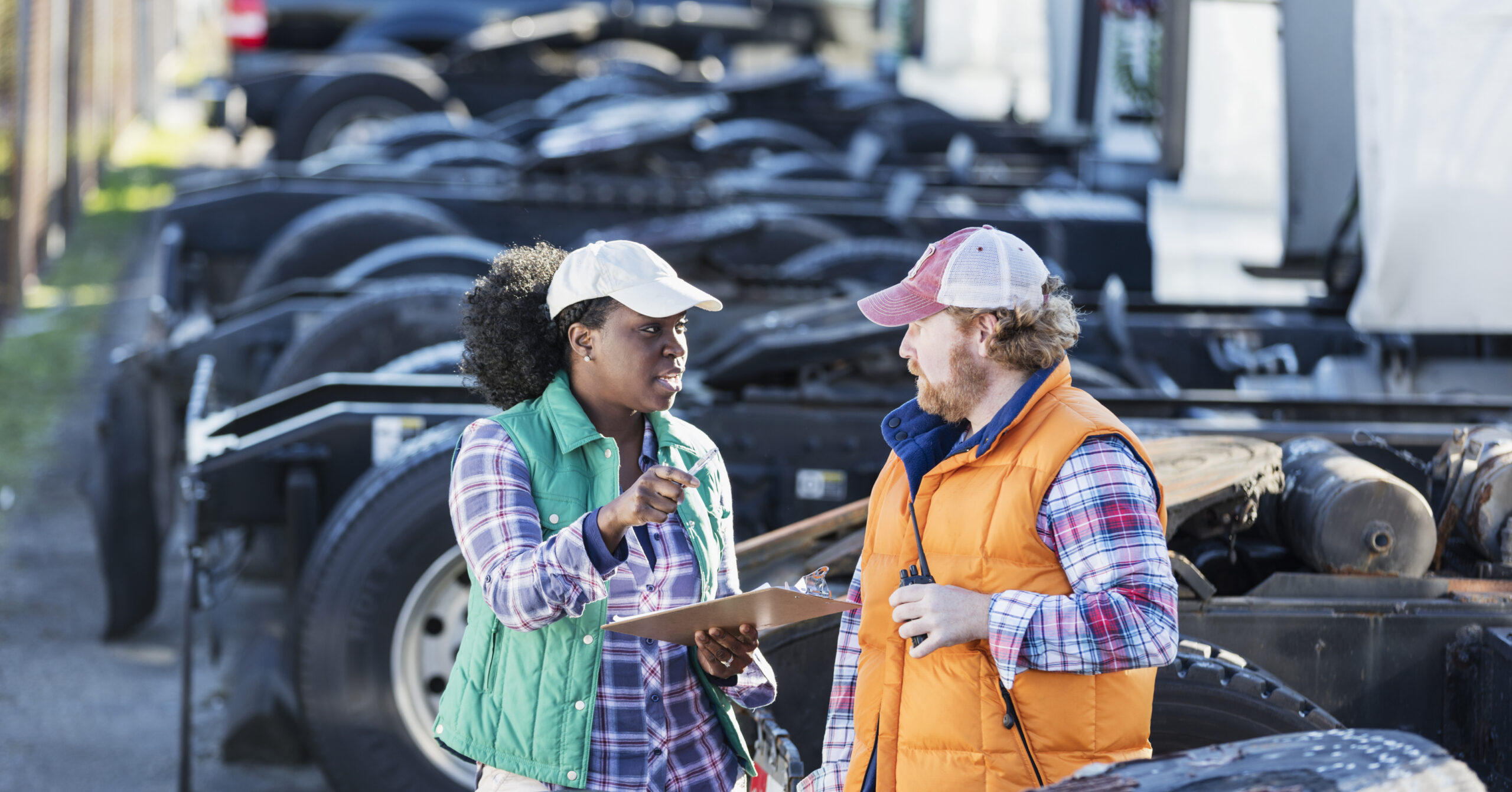 Two fleet workers review a clipboard beside commercial trucks.